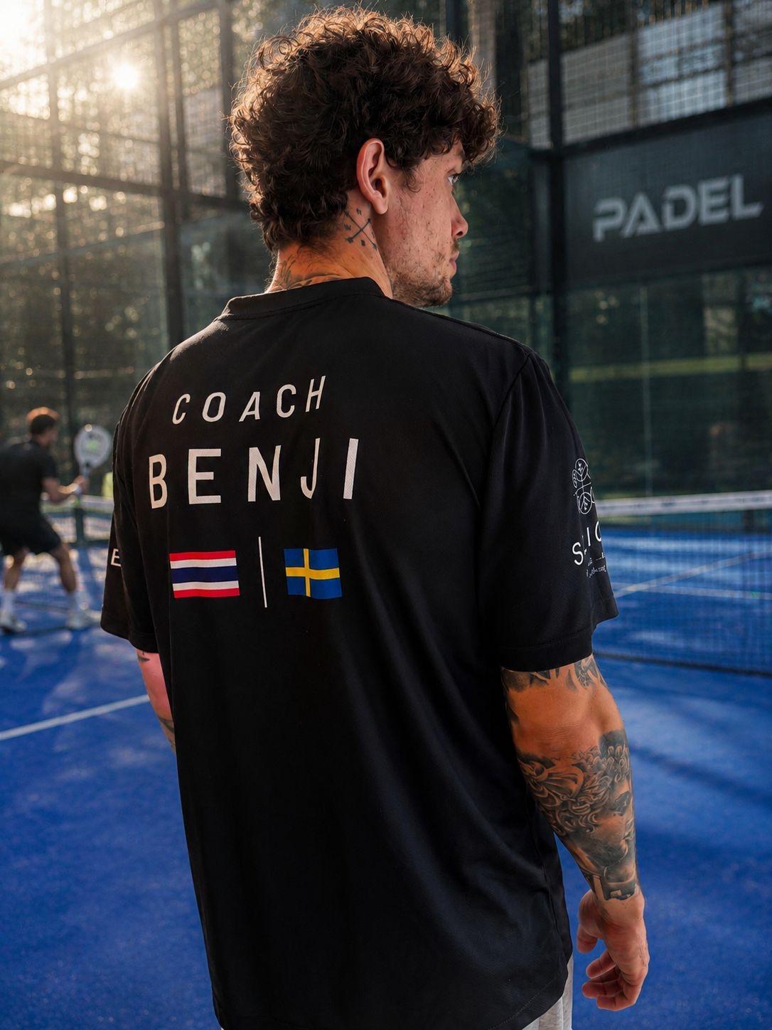 Coach Benji seen from behind on a blue padel court, 'COACH BENJI' printed on his shirt, golden backlight from the upper left.